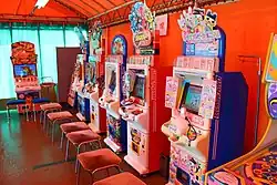 multiple pink game machines with chairs placed in front of them