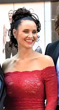 close-up of Barbora Řeháčková wearing a see-through red dress revealing a white bra, looking left of camera and grinning broadly with squinted eyes