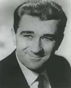 Black and white publicity shot of a smiling man with dark hair brushed back.