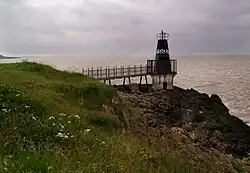 Metal lighthouse reached by walkway from land.
