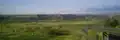 Photograph of the Bear River Massacre Site, a wide, open grassland with scattered trees, low hills in the background, and a highway alongside.