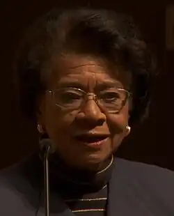 Head shot of a formally dressed Davis, who wears glasses, against a brown backdrop