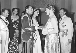 In the middle of a black and white photograph, two couples in uniform greet each other, while to the left other people in uniform observe the scene.