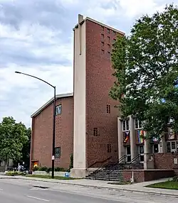 An asymmetrical, heavily massed red brick church with a tall, rectangular belltower in the center