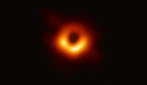 Over a black background of empty space, an orange-red donut of gas lies in the center of the image, with a black circle--the black hole's shadow--in the middle of the donut.