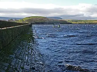 An image of an upland reservoir with choppy waves lapping at setts of stones on the left hand side