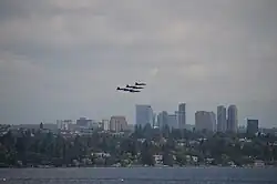 Six fighter planes fly in a tight triangle formation above city skyline on a cloudy day