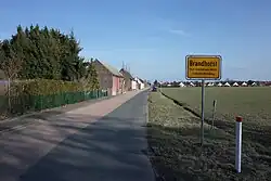 A road leading to a German village, with a yellow road sign saying "Brandhorst"