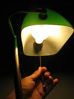 The bulb in the lamp generally emits warm light and is not colourful; any green cast comes from the light filtering through the lampshade.