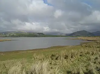 A view of Broad Water with grass in the foreground leading down to the shore, and hills in the background behind the lake.