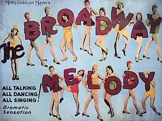 A poster with chorus girls in colorful costumes posing with large letters that spell out the film's title against a blue background.