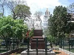 A statue in a plaza, with trees at the sides, and wires around it.