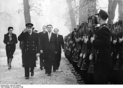politicians walk in snow, past an honour guard with rifles