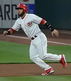 Eugenio Suárez running between first base and second base in a white Cincinnati Reds uniform