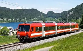 Red train with white stripes with a lake in the background