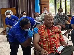 Physician injecting vaccine into seated man's shoulder