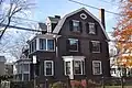 A large brown 3 story colonial style house with white trim and black shutters.