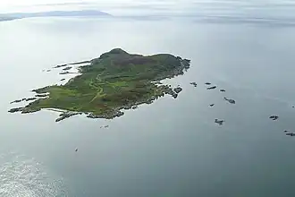 A green island sits in a calm sea. There are numerous small islets in the surrounding waters.