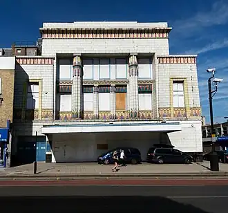 White-tiled building with Egyptian Revival decoration including colorful lotus-topped columns and geometric friezes above closed ground-floor entrance