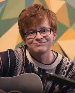 A person sitting on a couch with an acoustic guitar