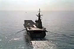 A small aircraft carrier photographed from behind as she sails across calm waters