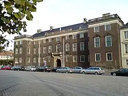 Three story palace with two large wings. Many decorative elements such as cornices, window pediments, and a stone balcony over the entrance.