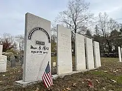A medium-gray rectangular grave marker with black text and a small American flag in front.