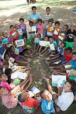Group of children sitting in a circle, holding picture books and smiling up at the camera