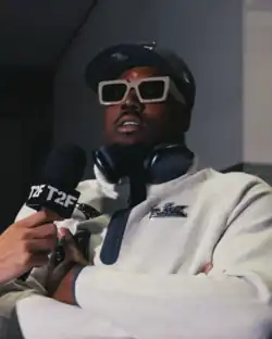 Headshot of Barmore in a white jacket, hat, and tinted glasses