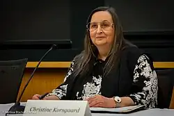 Photo of a woman wearing glasses and sitting at a table with a microphone