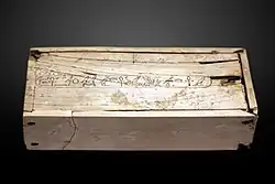 White rectangular box with small cracks and a long line of hieroglyphs along the entire length of the lid, at its centre