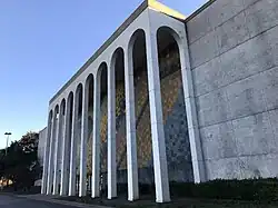 A large building with marble columns. A colorful, abstract mural is visible behind the columns.