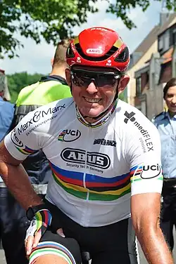 Man in white jersey with rainbow bands and a red helmet.