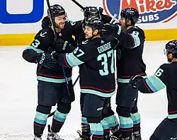 Multiple ice hockey players in Seattle Kraken jerseys surrounding each other
