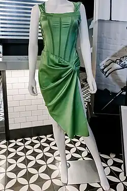Smart's green dress is displayed on a mannequin. It is made of satin with stripes of non-shiny matching fabric on the bodice, and the skirt is in a draped knot, with no rhinestones or other small decorations.