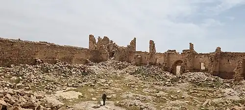 Qasr Bshir's courtyard is cluttered with fallen stones, interspersed with sparse patches of vegetation.