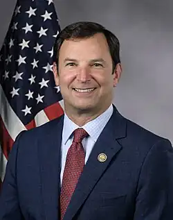 Official House portrait of Goldman smiling in front of the U.S. flag, wearing a blue jacket, light blue shirt, and checkered red tie.