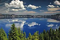 The water of Crater Lake can be seen above a forested area in the foreground.
