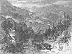 Sepia toned print shows soldiers marching through mountainous country.