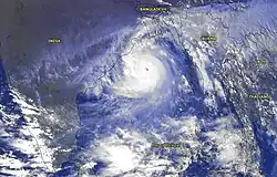 Satellite view looking over the Bay of Bengal, deliminated by India to its west, Bangladesh to its north, and Indochina to its west. Various patches of substantial storm tracts define the southern margins of the shot, but a larger buzzsaw-shaped whorl of clouds sits above the northern Bay, just beginning to impact parts of Orissa, West Bengal and Bangladesh.