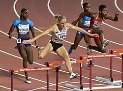 Photo of four athletes, two while approaching their hurdles and two while jumping over their hurdles