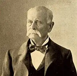 Head shot of an older man with white hair and moustache, dressed in tuxedo and bow tie.