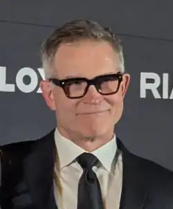 Cropped headshot of David Baszucki in a black suit and tie at an event called RDC 2025 with his wife Jan Ellison