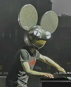 A man wearing a black mouse head-shaped helmet, a black T-shirt, and black pants, performing live