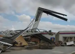 A white-and-red collapsed building with a large portion of wall sticking out of the ground above the rest of debris