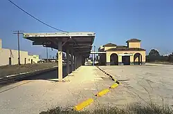 A one-story Mediterranean Revival building with yellow stucco walls and red tile roof. In the foreground is a steel canopy.