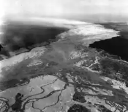 A black and white photograph of the lower course of the Delta River, showing various braided streams and a large cloud of silt blowing into the air