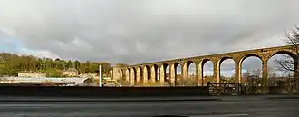 A curving stone viaduct bathed in sunshine on the right of the image; houses and a small valley are shown on the left