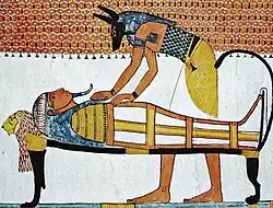 Painting of a jackal-headed god bending over a mummy on a bier