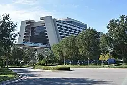 A view of Disney's Contemporary Resort, a modernist building with a monorail passing through its center and surrounded by Floridian foliage